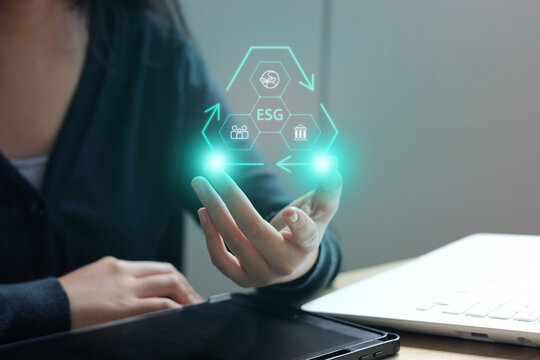 Woman Supporting Triangle ESG Hologram over her Open Hand next to Tablet and Laptop on Wooden Desk
