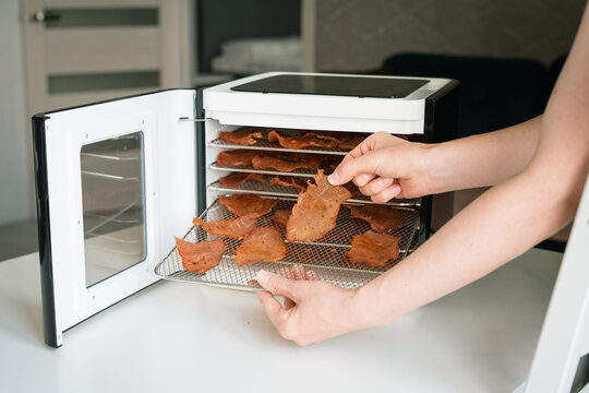 Hand holding jerky slices from dehydrator in modern kitchen  
