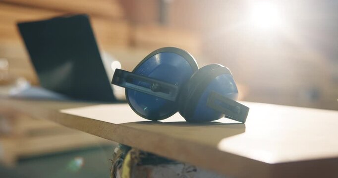 Earmuffs, carpentry and workshop with safety tools, woodwork and noise reduction tech. Laptop, flare and equipment on desk with ppe, ear protection and hearing damage prevention in joinery industry
