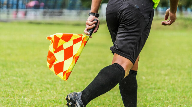 Assistant referee running with checkered flag during football match on outdoor soccer field