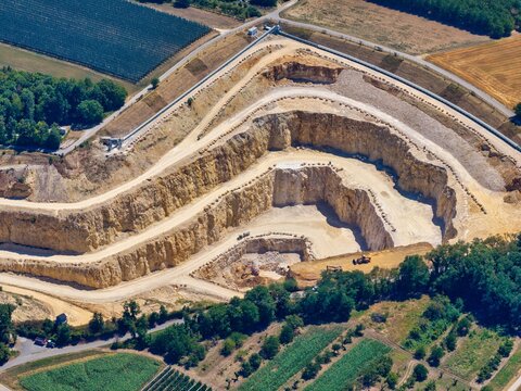 Aerial view of the limestone quarry in Kembs featuring terraced excavation levels and heavy machinery surrounded by agricultural fields and forests in Kembs, Grand Est, France.