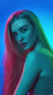 Young woman with animated facial tracking grid in colorful neon beauty portrait. Concept of biometric skincare analysis, augmented beauty technology, futuristic cosmetics advertising.