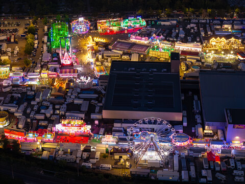 Aerial view of the illuminated Parc Expo Mulhouse fairground at night, featuring a glowing Ferris wheel, colorful amusement rides, and surrounding parking areas in Mulhouse, Grand Est, France.