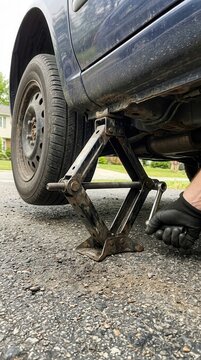 A close-up perspective of a mechanical scissor jack lifting a vehicle for tire replacement