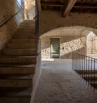 The covered entrance to an old house that has been completely renovated, with stone walls.  In the centre is a glass door. To the left, an old staircase leading up to the upper floor.