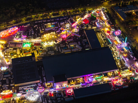 Aerial view of the illuminated Parc Expo Mulhouse at night, featuring vibrant fairground rides, exhibition halls, and glowing lights in Mulhouse, Grand Est, France.