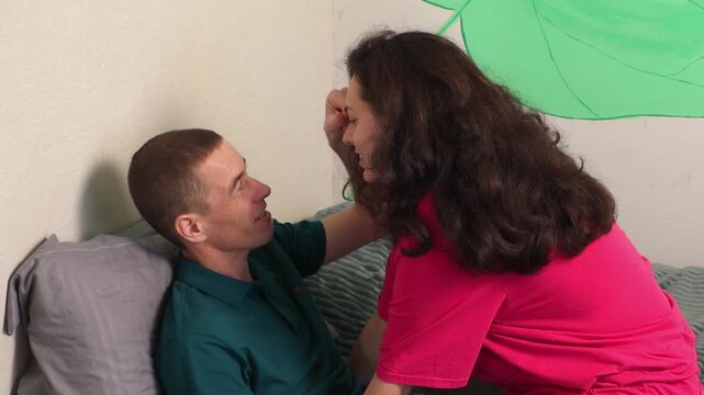 Young man and woman cuddling on a bed and enjoying carefree moments together. Their affectionate interaction highlights romance, tenderness, and emotional wellbeing in a home environment.