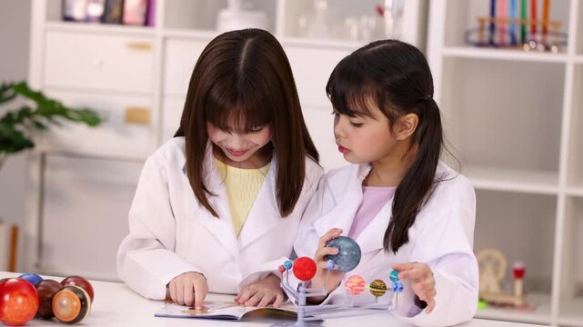 Asian Schoolgirls in Lab Coats Studying Solar System Model in Classroom