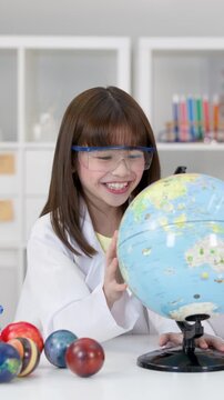 Young Girl in Lab Coat Spinning Globe in Science Classroom