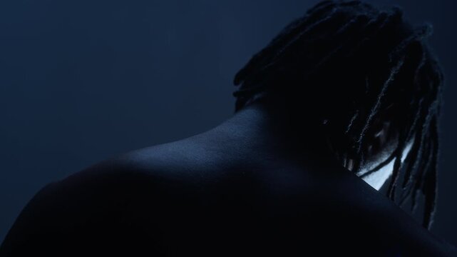 African American young adult man standing with his head bowed against datk background, slow motion. Footage ideal for mental health awareness or fashion concepts