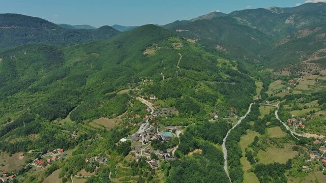 Aerial view of Drvengrad Kustendorf ethno village on Mokra Gora, Serbia, surrounded by green hills and mountains, 4k