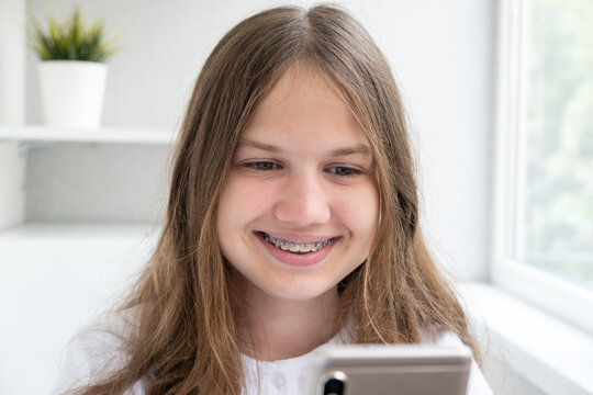 Happy beautiful teen girl with dental braces on teeth holding mobile phone texting using mobile app. Smiling teenager in brackets using smartphone