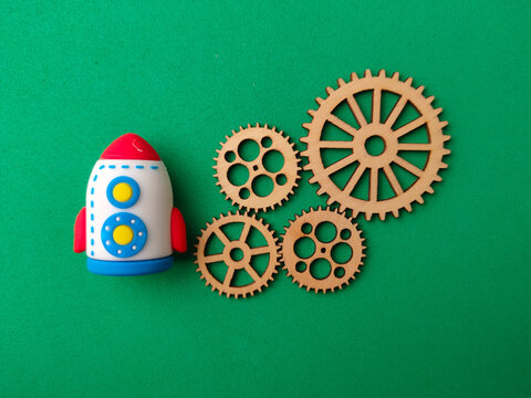 A colorful toy rocket positioned beside four wooden gear cogs on a bright green background
