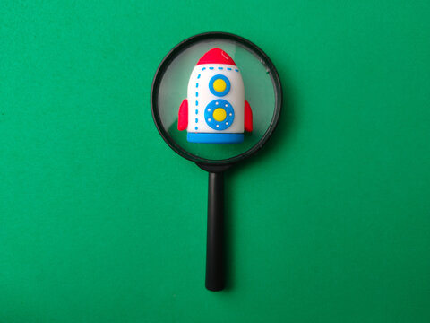 A miniature toy rocket viewed through a black magnifying glass centered on a green background