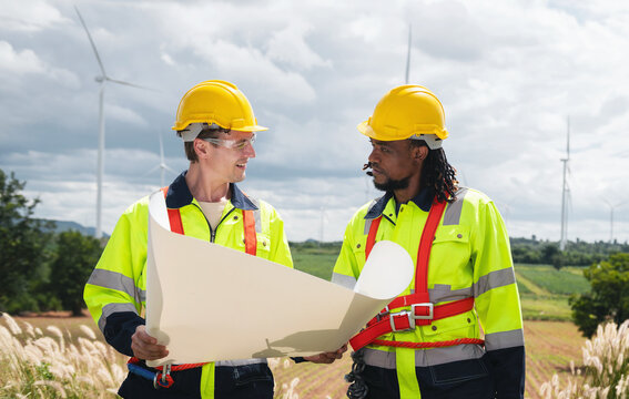 Two engineers stand outdoors, holding blueprints