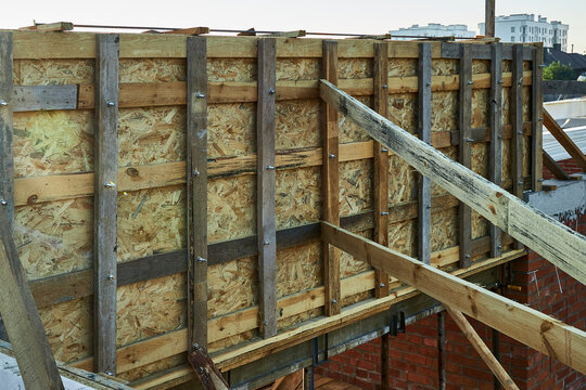 Horizontal view of custom wooden formwork panels made of OSB boards, timber studs, and steel threaded rods, prepared for pouring a concrete beam on top of a brick wall.