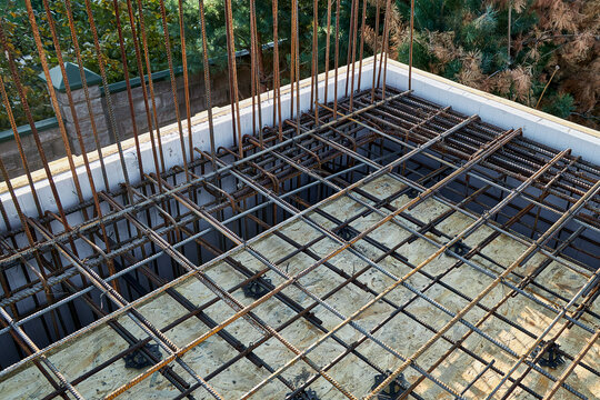 High-angle horizontal shot of a tied steel reinforcement rebar grid with plastic spacers and vertical starter bars, laid over OSB formwork for a concrete slab corner casting.