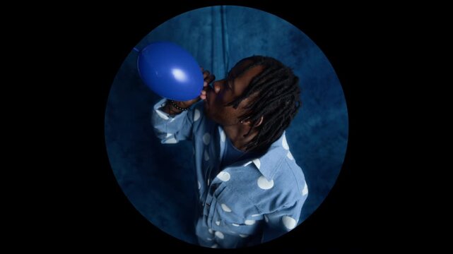 African American young adult man blowing up blue balloon and letting it fly away. Clip is ideal for party planning advertisements, mental health concepts, or creative lifestyle marketing campaigns