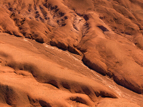 Aerial view of the arid, undulating landscape of the Atacama Desert with deep erosion channels and reddish-brown terrain in Atacama, Chile.