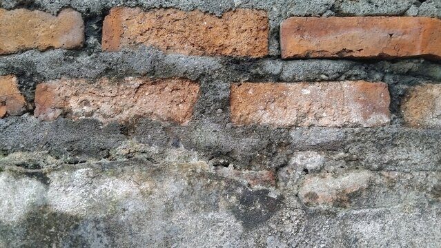 ​Close-up of old weathered red brick wall with rough cement mortar texture