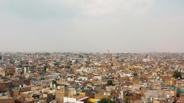 High angle aerial drone shot of a dense Asian urban city skyline with packed residential brick houses and rooftops under a hazy afternoon sky.
