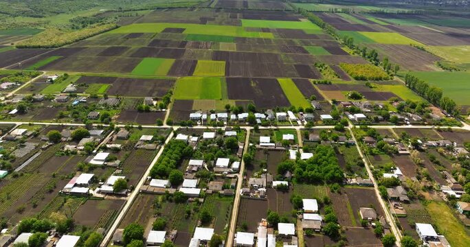 Aerial motion shot of a small village with residential houses and surrounding agricultural fields under a dramatic cloudy sky.