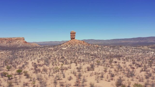 Drone panorama of Fingerklippe rock needle, Namibia. Towering formation rises from dry terrain. Barren leafless trees, clear cloudless midday sky footage
