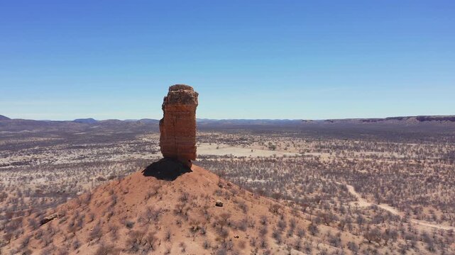 Slow panoramic drone passes Fingerklippe rock needle, Namibia at midday. Dry terrain, barren leafless trees, clear cloudless sky