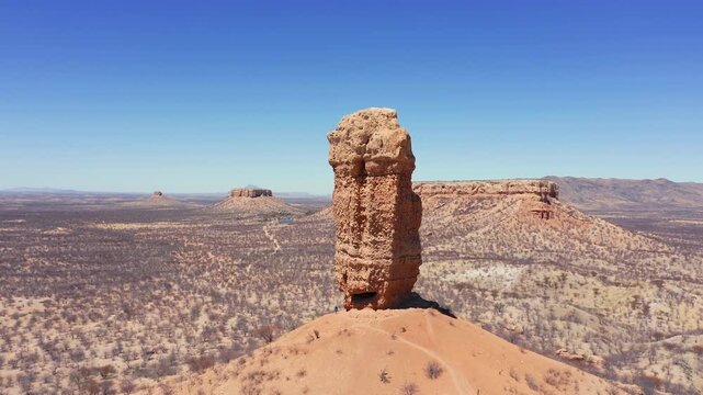 Slow panoramic drone pan of Vingerklip rock formation, Namibia. Towering needle rises from dry landscape. Leafless trees, clear cloudless sky
