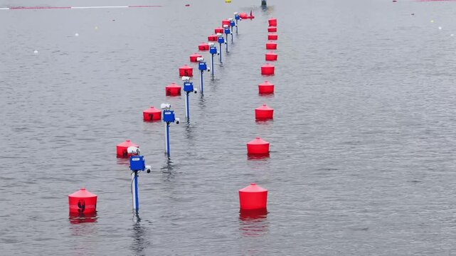 Canoe sprint course markers on a Brandenburg lake, with red lane buoys, blue timing posts, 200 meter sign and calm grey race water.
