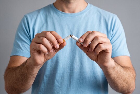 A man in a blue t-shirt snapping a cigarette in half, symbolizing the choice to quit smoking, break an addiction, and commit to a healthier lifestyle.