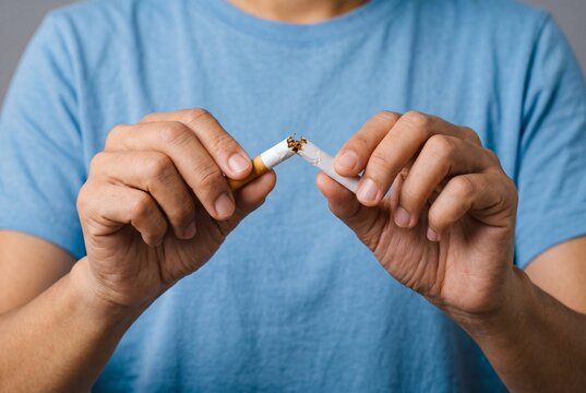A person in a blue t-shirt breaking a cigarette in half as a symbol of quitting smoking and choosing a healthier lifestyle.