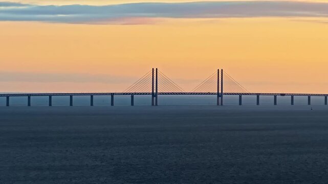 Iconic Oresund bridge connecting Denmark and Sweden over calm ocean at sunset.
