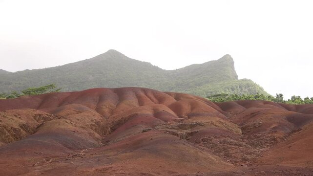 Striking dunes of the iconic Chamarel Seven Coloured Earth geopark in Mauritius, showcasing vibrant mineral-rich sand layers against a lush green backdrop.