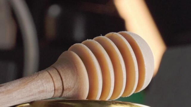 Close up of a wooden honey dipper resting on a glass jar of golden honey, highlighting natural sweetness, beekeeping and organic food ingredients.