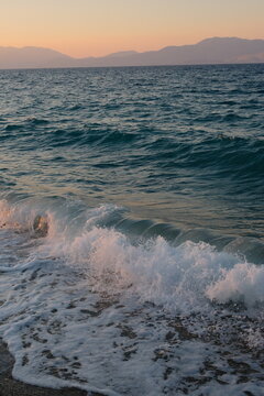 Sea waves foaming on shoreline at sunset with distant mountains