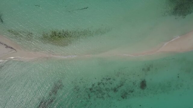 Aerial view of tropical sandbar with turquoise water and shallow sea textures, drone overview of water splashing and closing out the isthmus