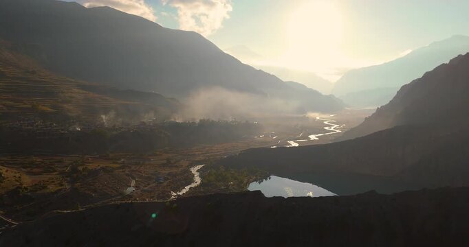Annapurna Circuit, Manang Nepal, gliding drone shot over Gangapurna Lake and Marsyangdi River winding through mountain valley at sunrise.