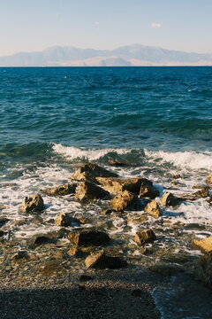 Rocky shoreline with waves breaking at sea and distant mountains