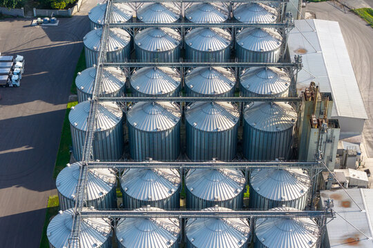 Aerial view of modern feed production and grain procurement facility featuring rows of metallic grain silos and parked trucks in Poland.