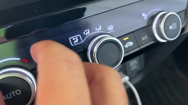 Close up of a hand adjusting the climate control knob on a vehicle dashboard, changing airflow settings on the car air conditioning control panel.