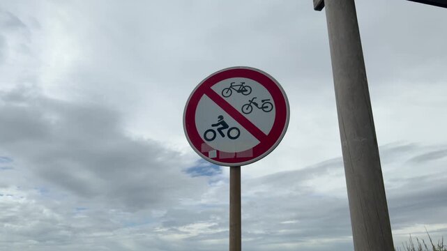 Red and white prohibition sign banning bicycles mopeds and motorcycles under cloudy sky
