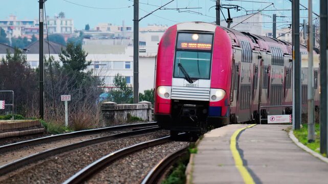 Modern commuter train arriving at railway station platform on rural route during daytime.