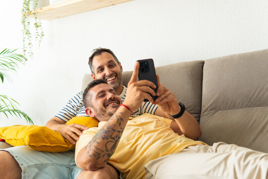 Gay couple relaxing on couch using smartphone together