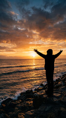Fototapeta premium Silhouette of a person with outstretched arms facing a dramatic sunset over the ocean, symbolizing freedom, reflection, and awe