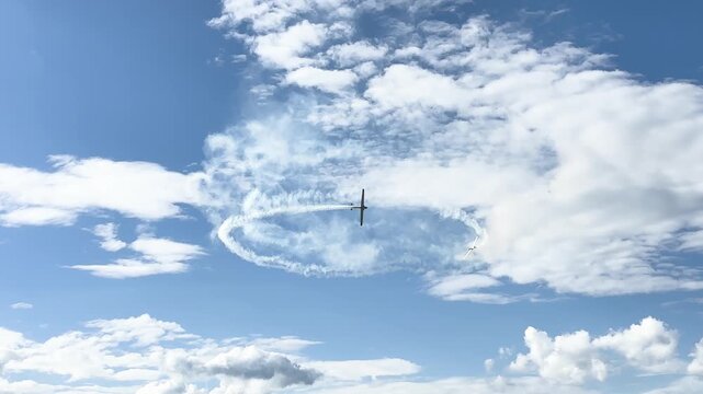 Airplane performing circular aerobatic maneuver with smoke trail in cloudy sky