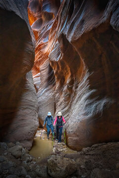 Couple navigating through water pools from recent rain, walking among towering narrow canyon. Buckskin Gulch. Utah. USA.