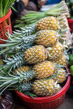 Pile of fresh ripe pineapples stacked in basin selling at street food market in Southeastern Asia, tropical organic fruits on display at vendor stall, local farmers growing and selling exotic produce.