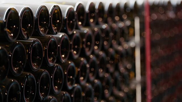 Rows of stacked wine bottles stored in horizontal metal racks at traditional winery cellar for aging process.
