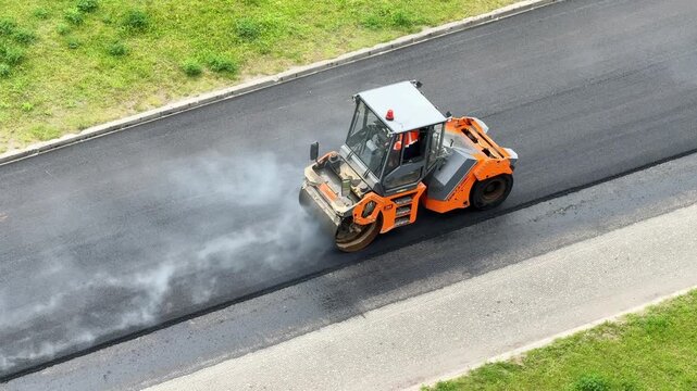 Compaction roller finishes fresh asphalt on a multilane highway, road modernization, industrial engineering, transport infrastructure, aerial construction view.
